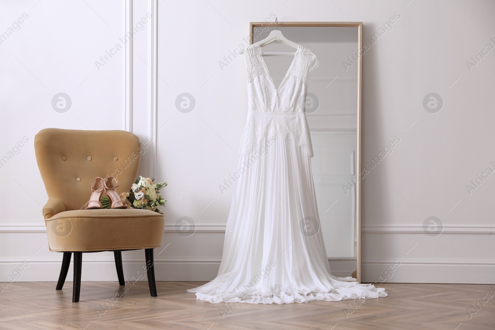 Photo of Elegant wedding dress hanging on large mirror in room