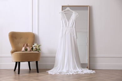 Elegant wedding dress hanging on large mirror in room