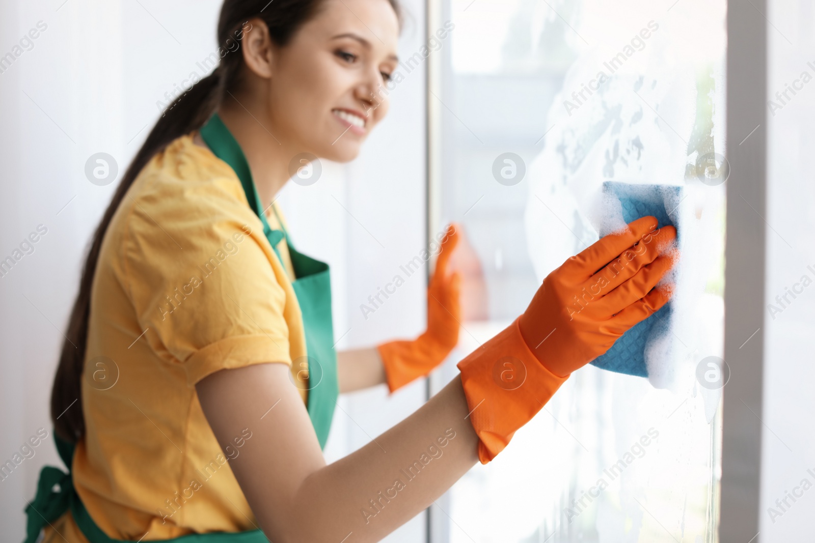 Photo of Young woman cleaning window glass at home