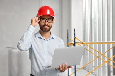 Photo of Professional engineer in hard hat with laptop indoors