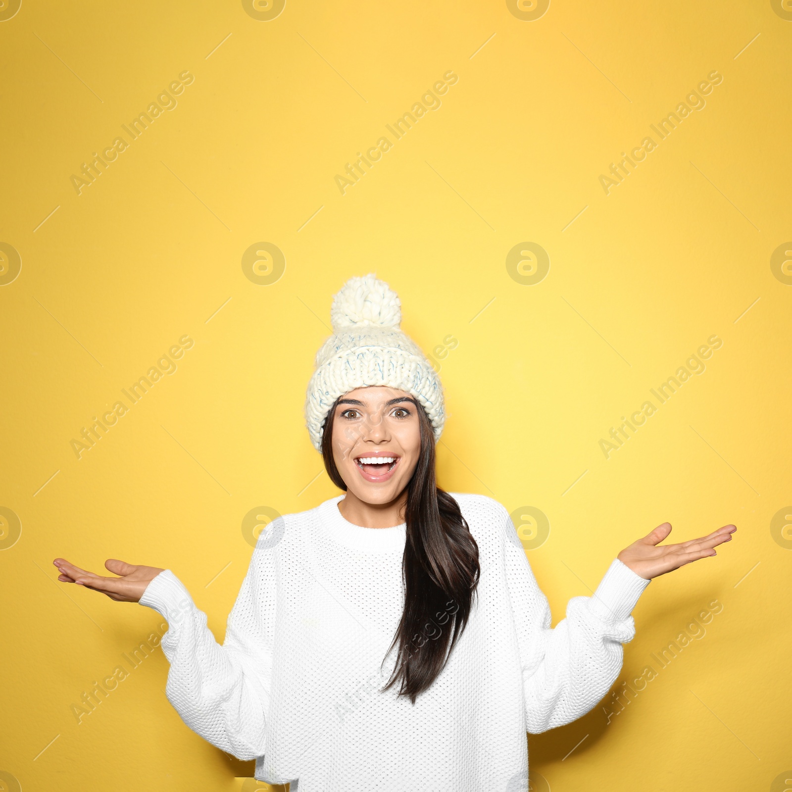 Photo of Young woman in warm sweater with hat on yellow background