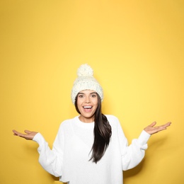 Young woman in warm sweater with hat on yellow background