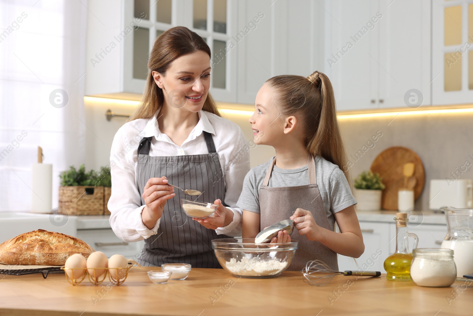 Photo of Making bread. Mother and her daughter putting flour and dry yeast into bowl at wooden table in kitchen