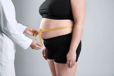 Photo of Doctor measuring fat woman's waist on grey background. Weight loss