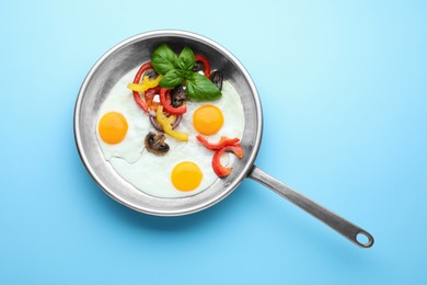 Photo of Tasty fried eggs with vegetables in pan on turquoise background, top view