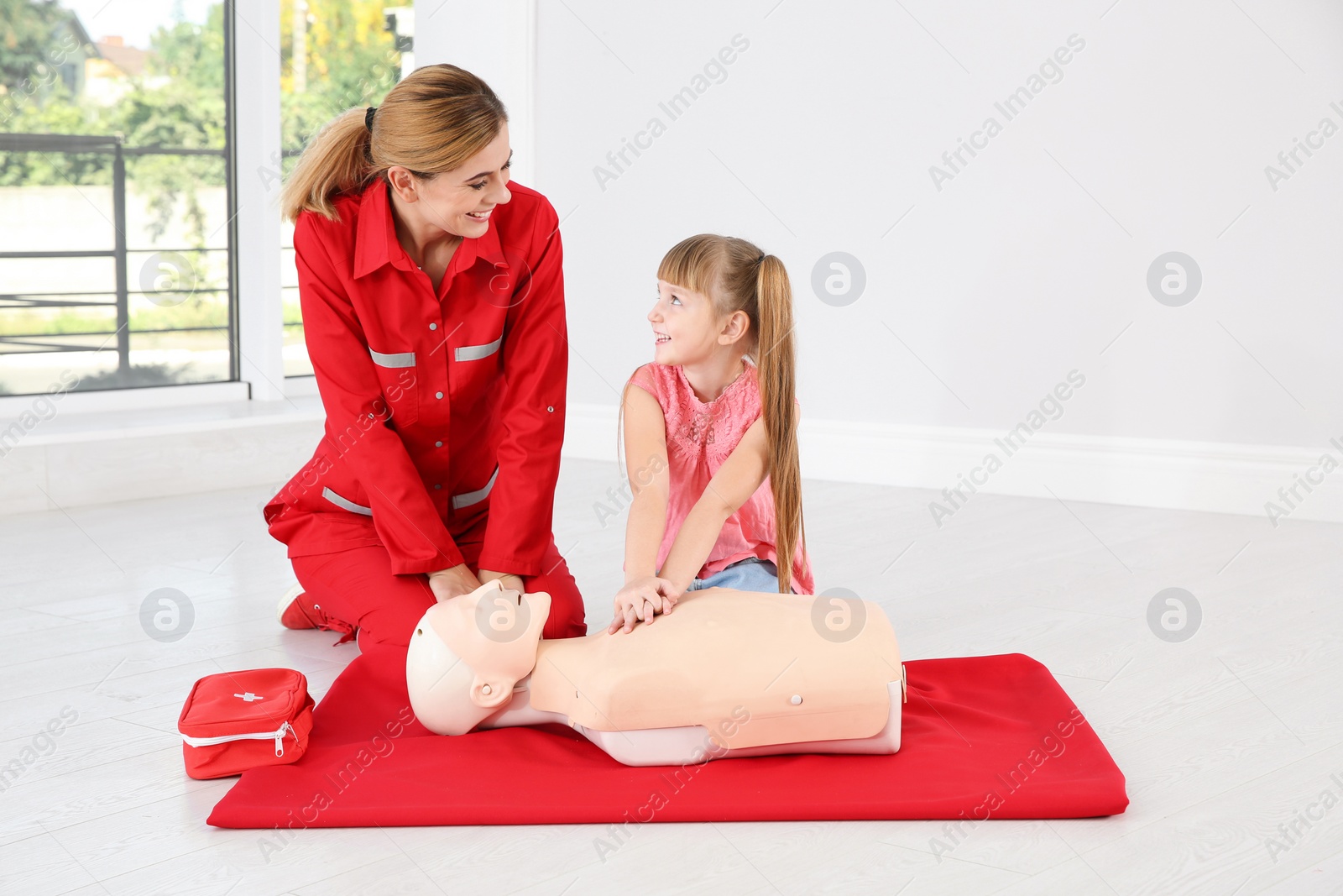 Photo of Instructor with little girl practicing first aid on mannequin indoors