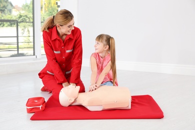 Photo of Instructor with little girl practicing first aid on mannequin indoors