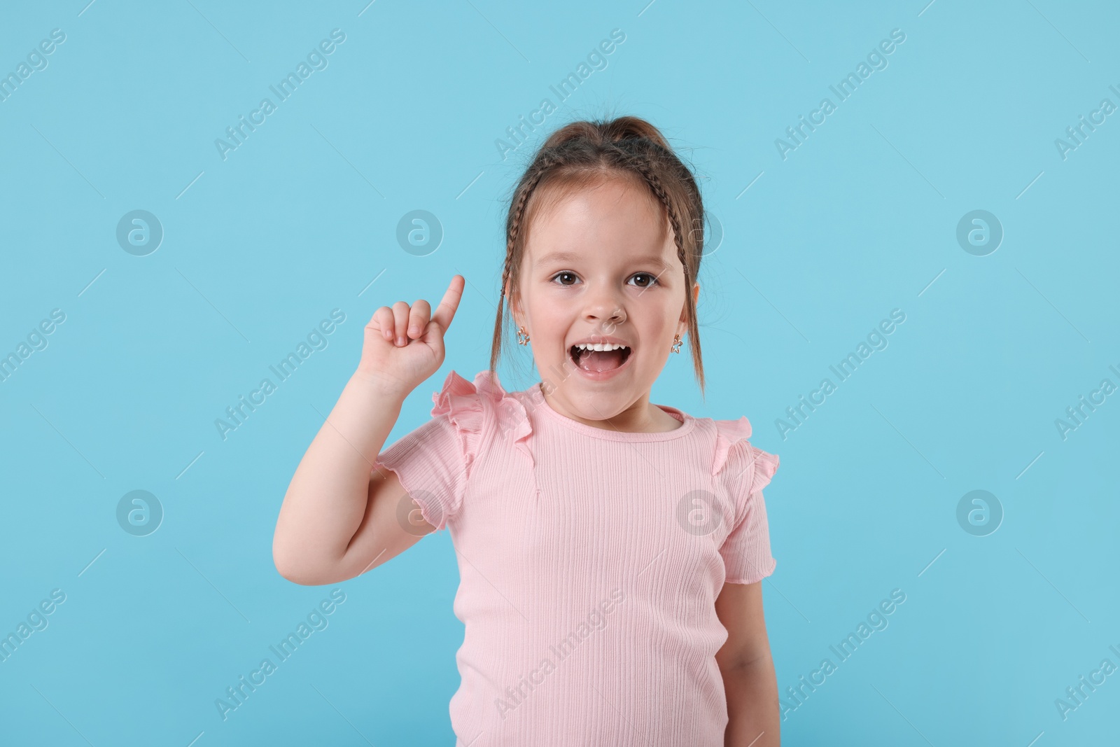 Photo of Cute little girl pointing at something on light blue background