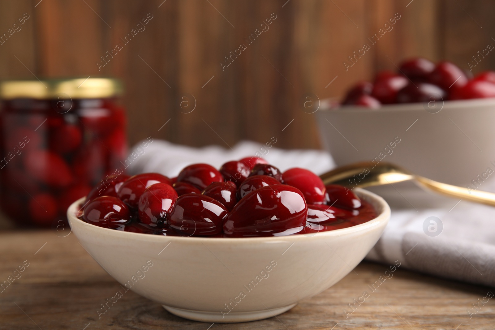 Photo of Delicious dogwood jam with berries in bowl on wooden table, closeup