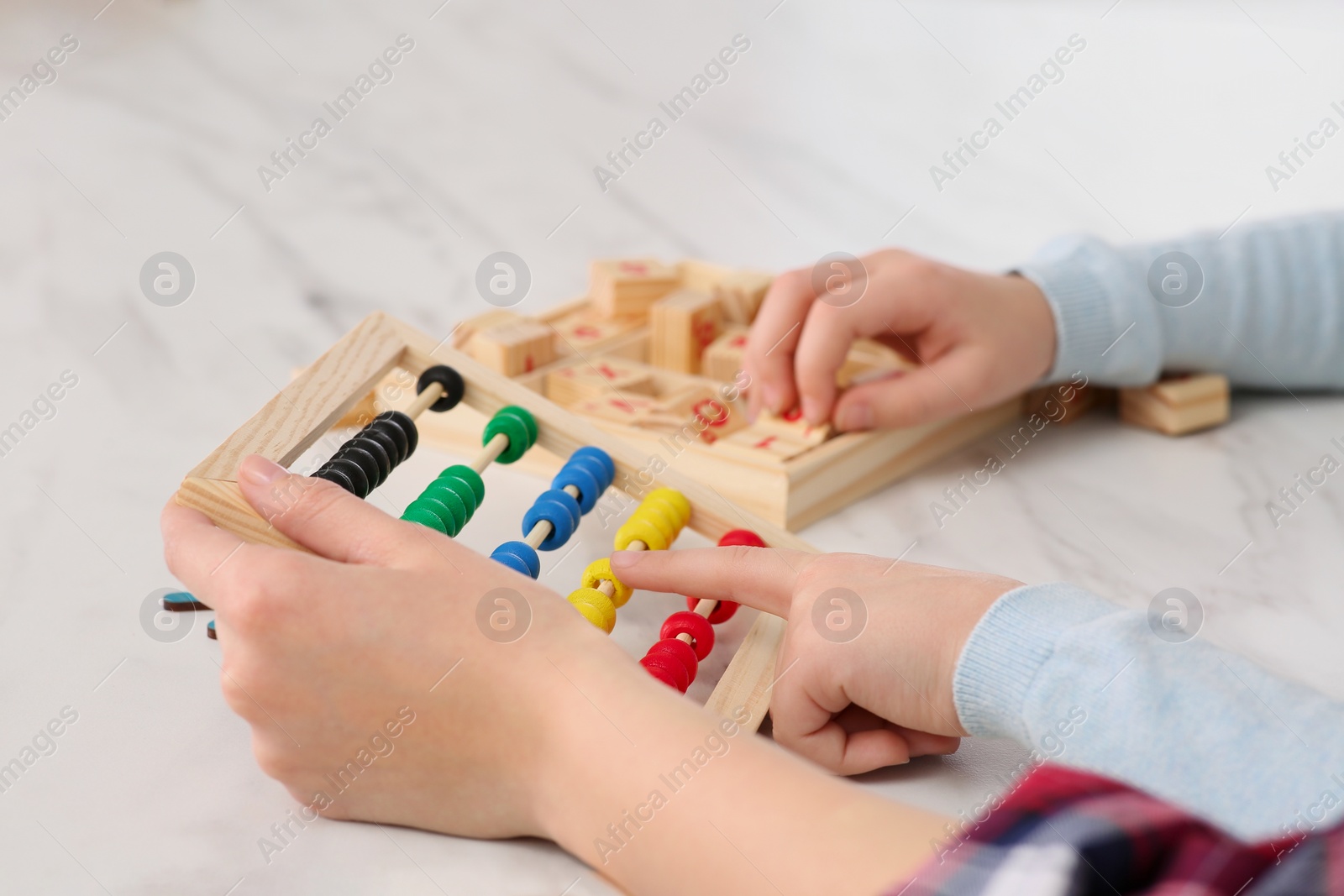 Photo of Mother and daughter playing with different math game kits at white marble table, closeup. Study mathematics with pleasure