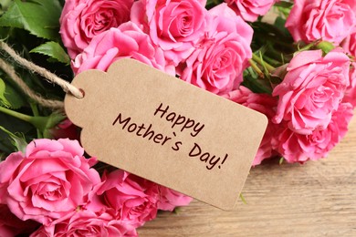 Image of Happy Mother's Day greeting label and beautiful rose flowers on wooden table