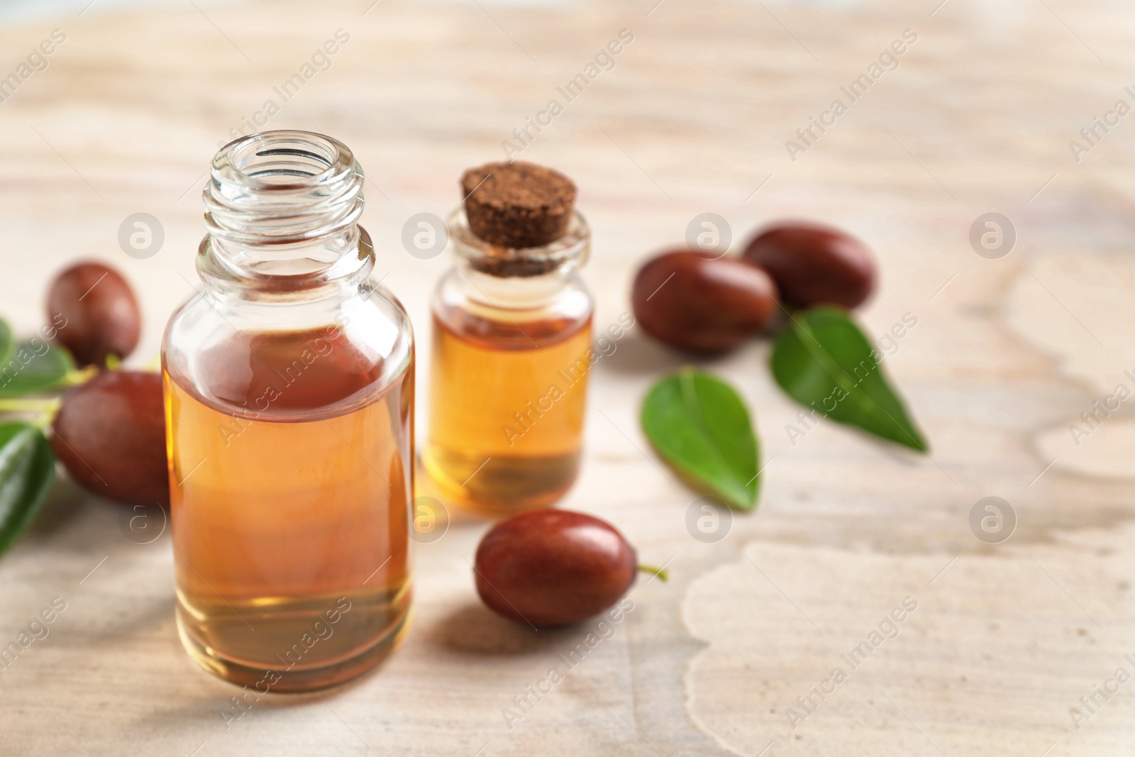 Photo of Glass bottles with jojoba oil and seeds on light table