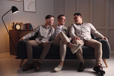 Photo of Happy groom and groomsmen sitting on sofa in room