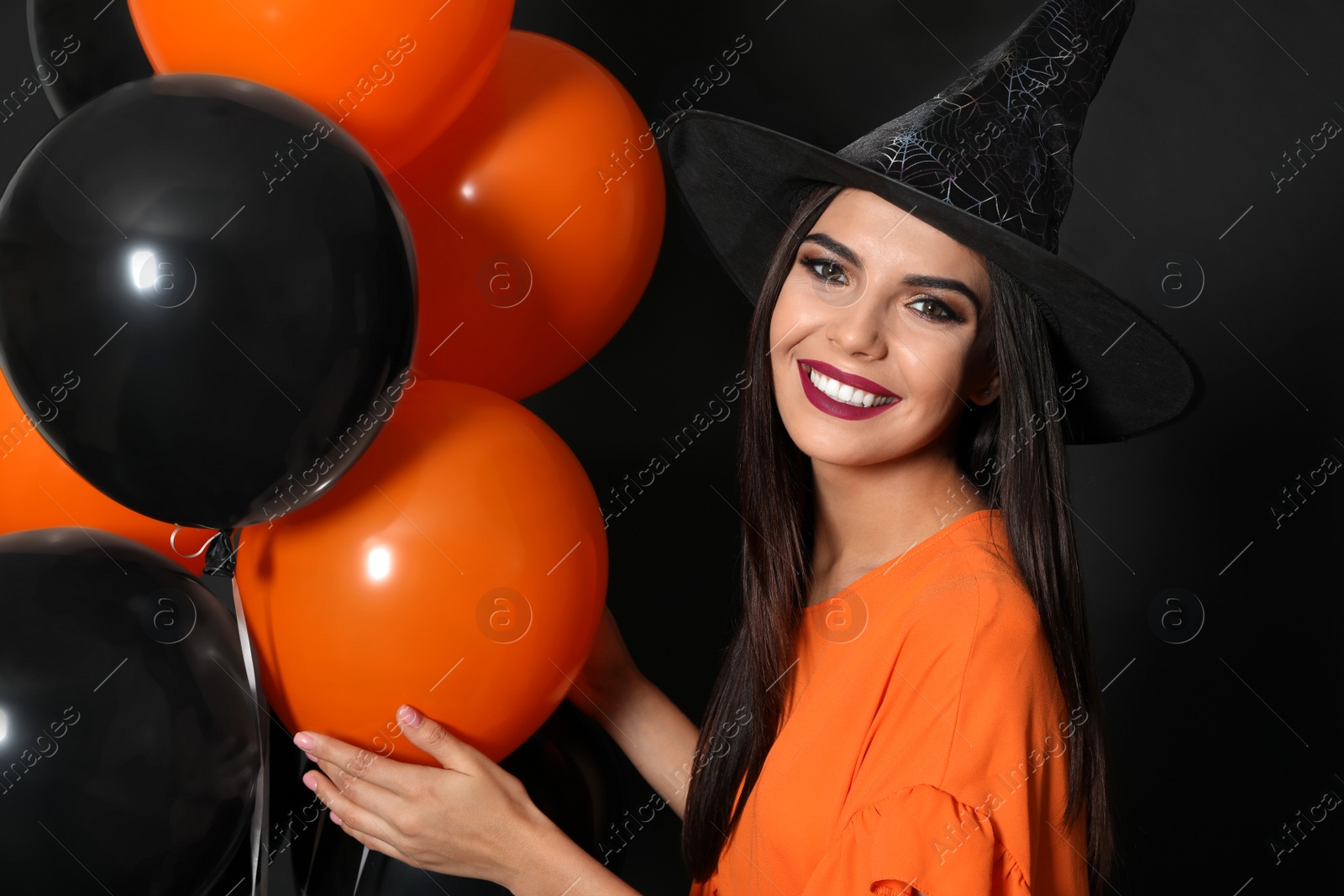 Photo of Beautiful woman wearing witch costume with balloons for Halloween party on black background