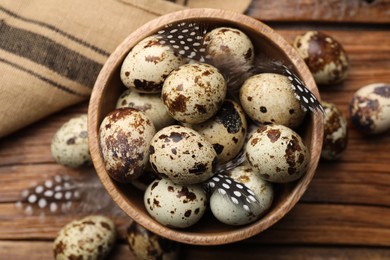 Speckled quail eggs and feathers on wooden table, top view