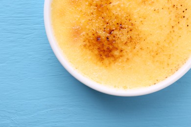 Delicious creme brulee in bowl on light blue wooden table, top view