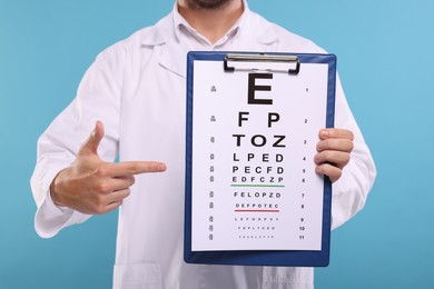 Ophthalmologist pointing at vision test chart on light blue background, closeup