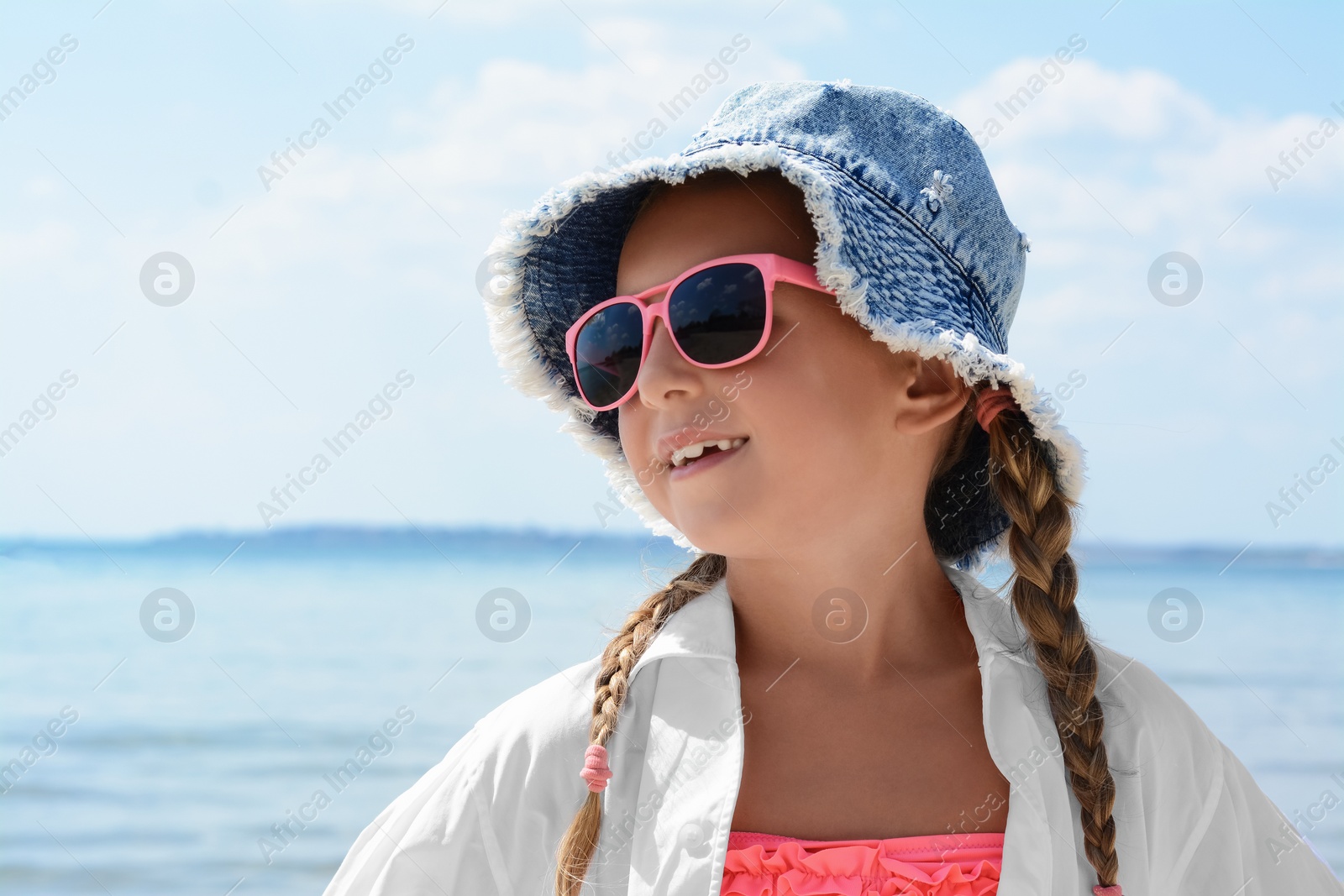 Photo of Little girl wearing sunglasses and hat at beach on sunny day