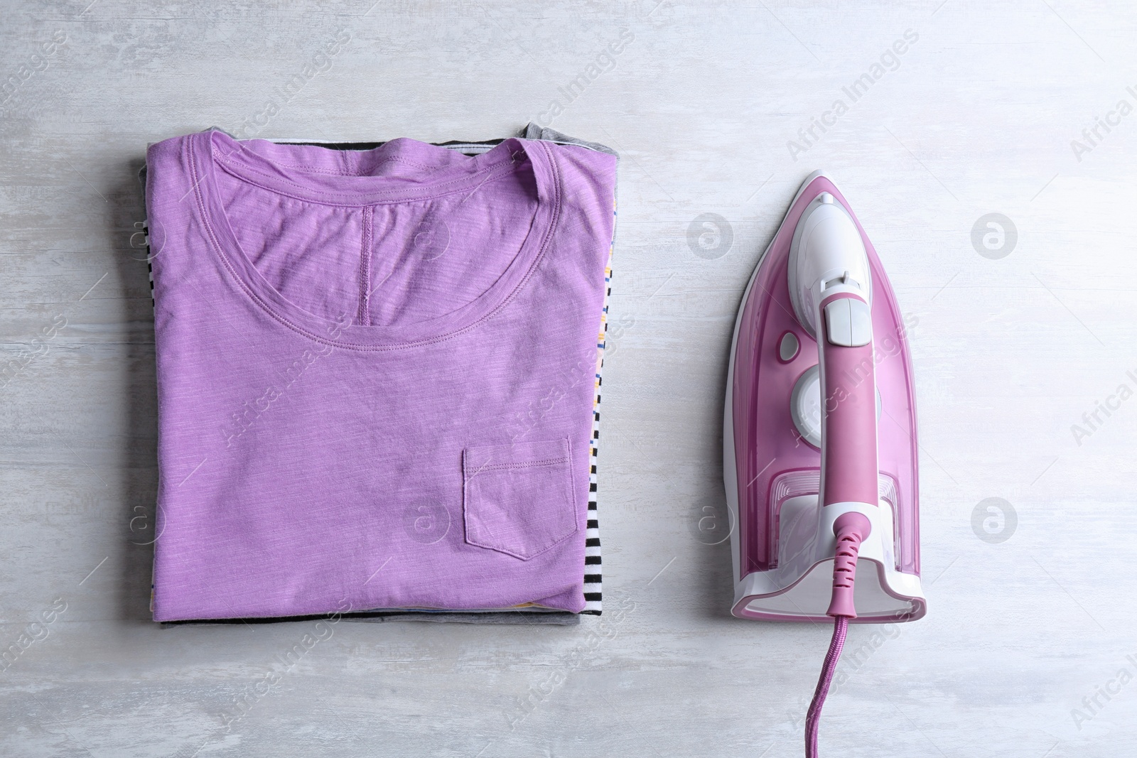 Photo of Flat lay composition with folded clothes and modern iron on light table