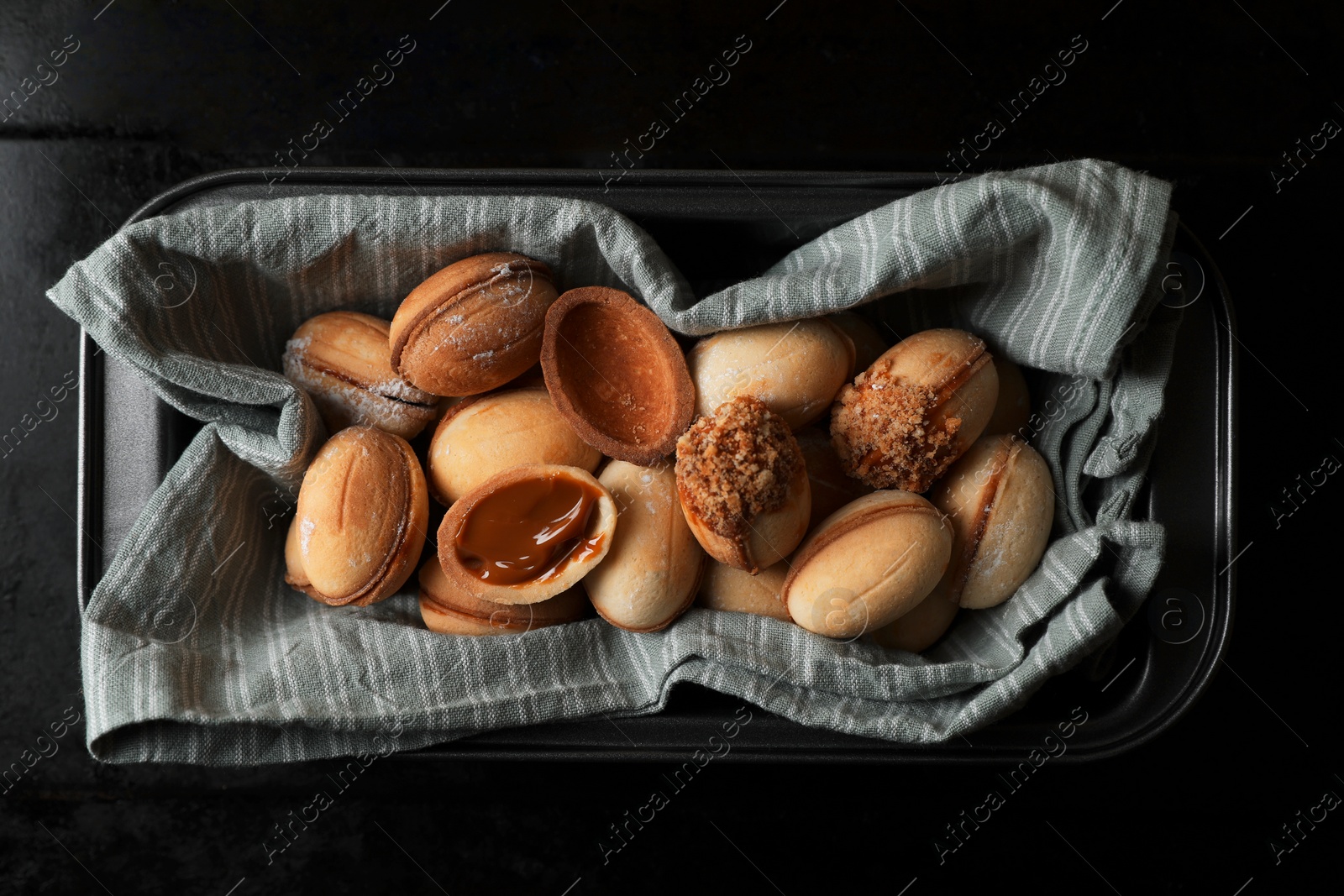 Photo of Freshly baked homemade walnut shaped cookies with condensed milk on black table, top view