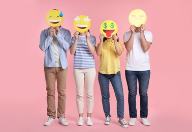 People covering faces with emoticons on pink background
