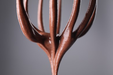 Chocolate cream flowing from whisk on grey background, closeup