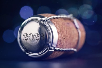 Image of Cork of sparkling wine and muselet cap with engraving 2023 on dark background, closeup. Bokeh effect