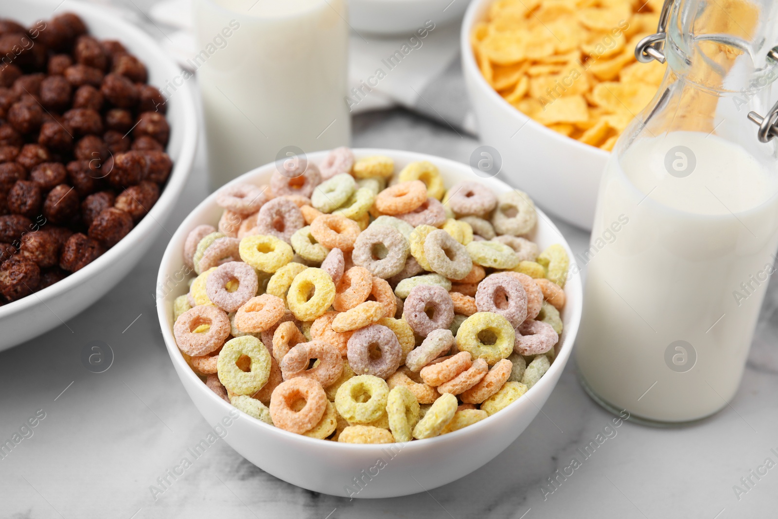 Photo of Different delicious breakfast cereals and milk on white marble table, closeup