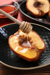 Pouring honey onto tasty baked quince in bowl at wooden table, closeup