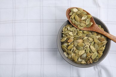 Photo of Bowl with pumpkin seeds and wooden spoon on tablecloth, top view. Space for text