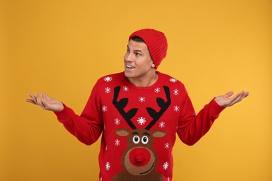 Emotional man in Christmas sweater and hat on yellow background