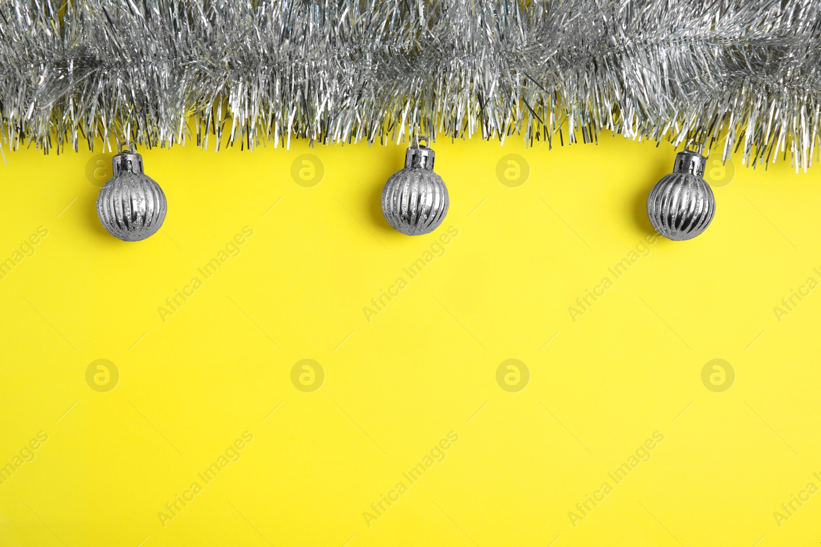 Photo of Silver tinsel and Christmas balls on yellow background, flat lay. Space for text