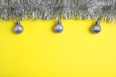 Silver tinsel and Christmas balls on yellow background, flat lay. Space for text