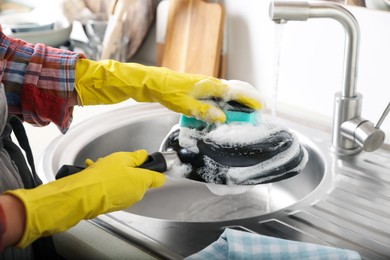 Photo of Woman washing dirty frying pan in sink indoors, closeup