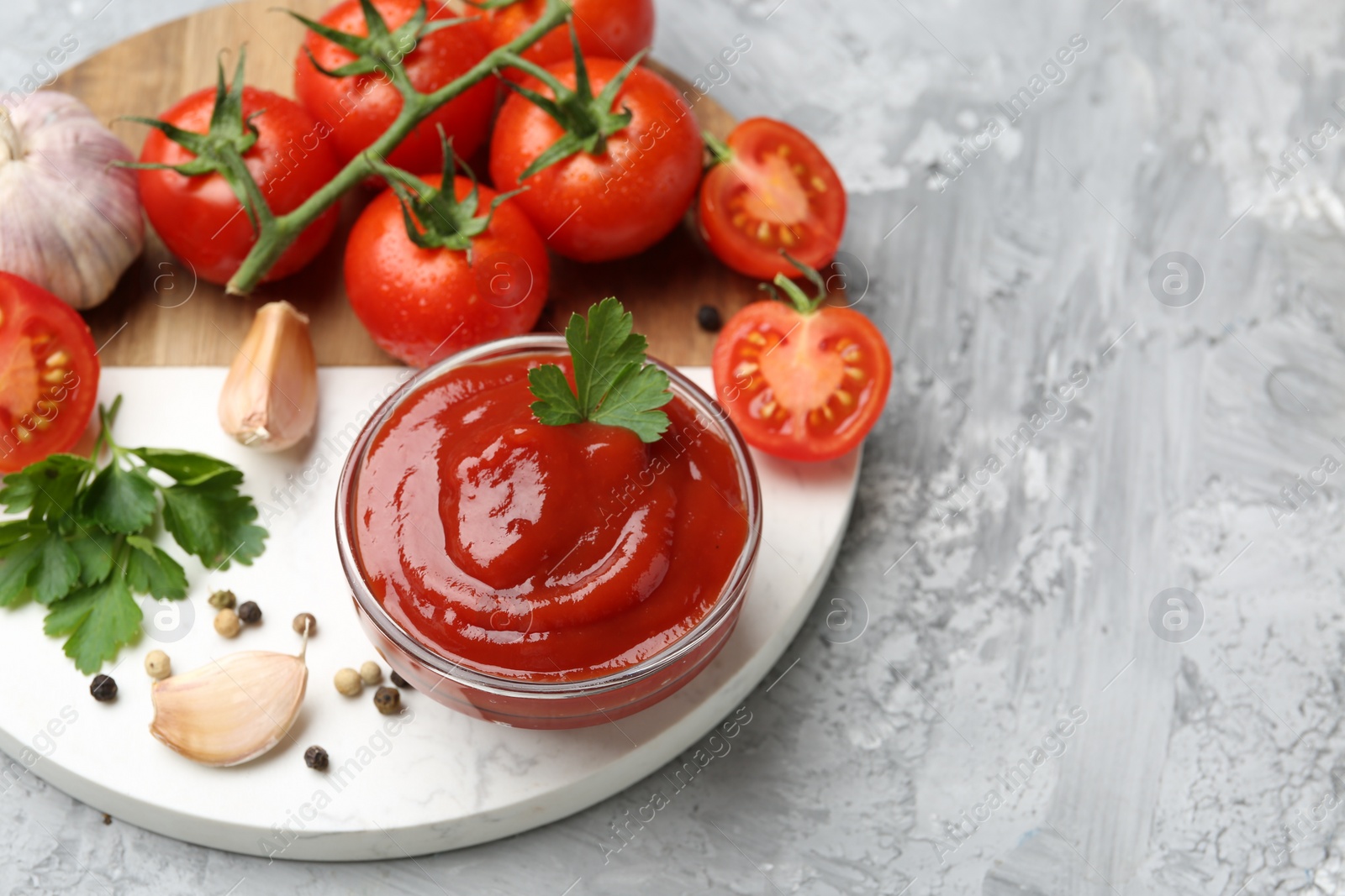 Photo of Delicious ketchup in bowl, parsley, garlic and tomatoes on grey textured table, above view. Space for text