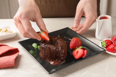 Photo of Chef decorating delicious fresh chocolate fondant with strawberry at table. Lava cake recipe