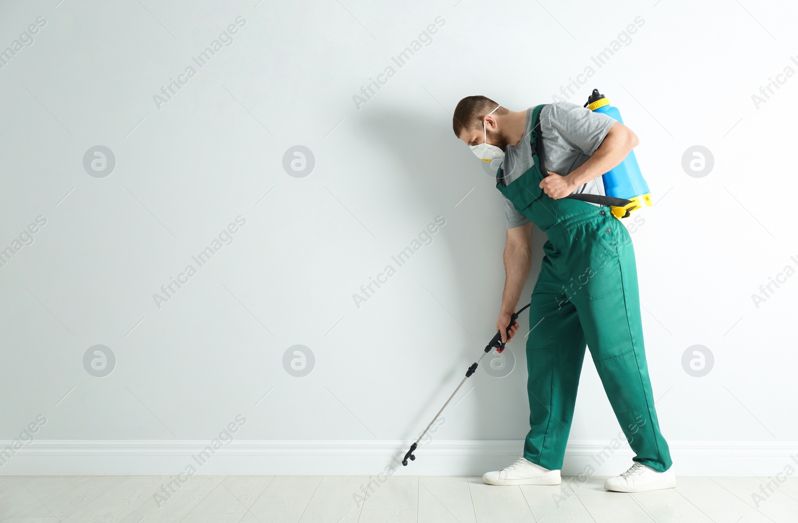 Photo of Pest control worker in uniform spraying pesticide indoors. Space for text