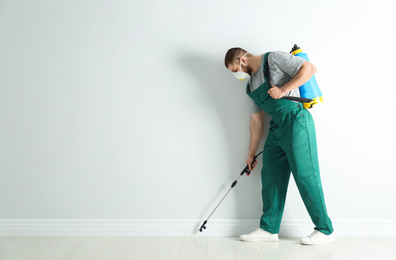 Pest control worker in uniform spraying pesticide indoors. Space for text