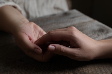 Photo of Woman holding hands with her mother at wooden table, closeup