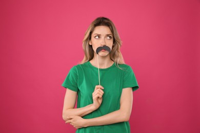 Young woman with fake mustache on pink background