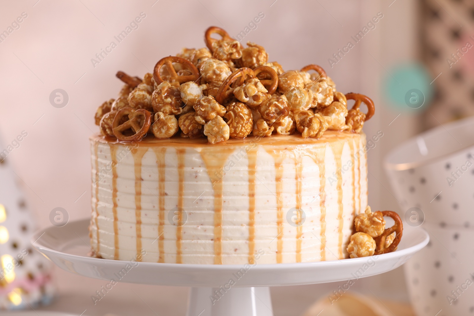 Photo of Caramel drip cake decorated with popcorn and pretzels against blurred background, closeup