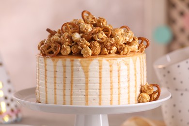 Photo of Caramel drip cake decorated with popcorn and pretzels against blurred background, closeup