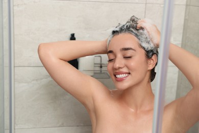 Beautiful happy woman washing hair with shampoo in shower