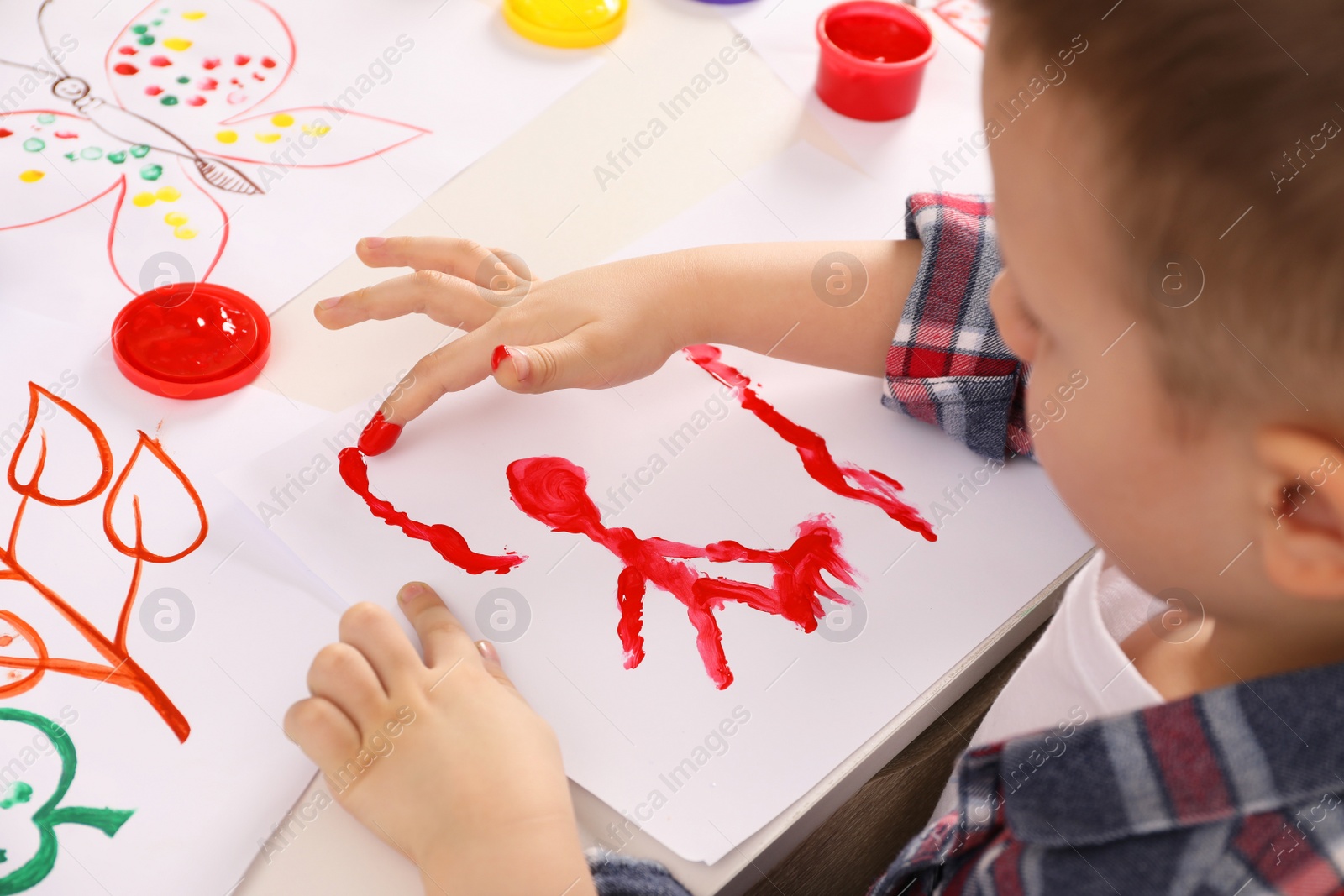 Photo of Little boy painting with finger at white table, closeup