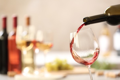 Photo of Pouring red wine from bottle into glass on blurred background. Space for text