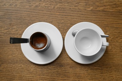 Jezve with fresh coffee and empty cup on wooden table, flat lay