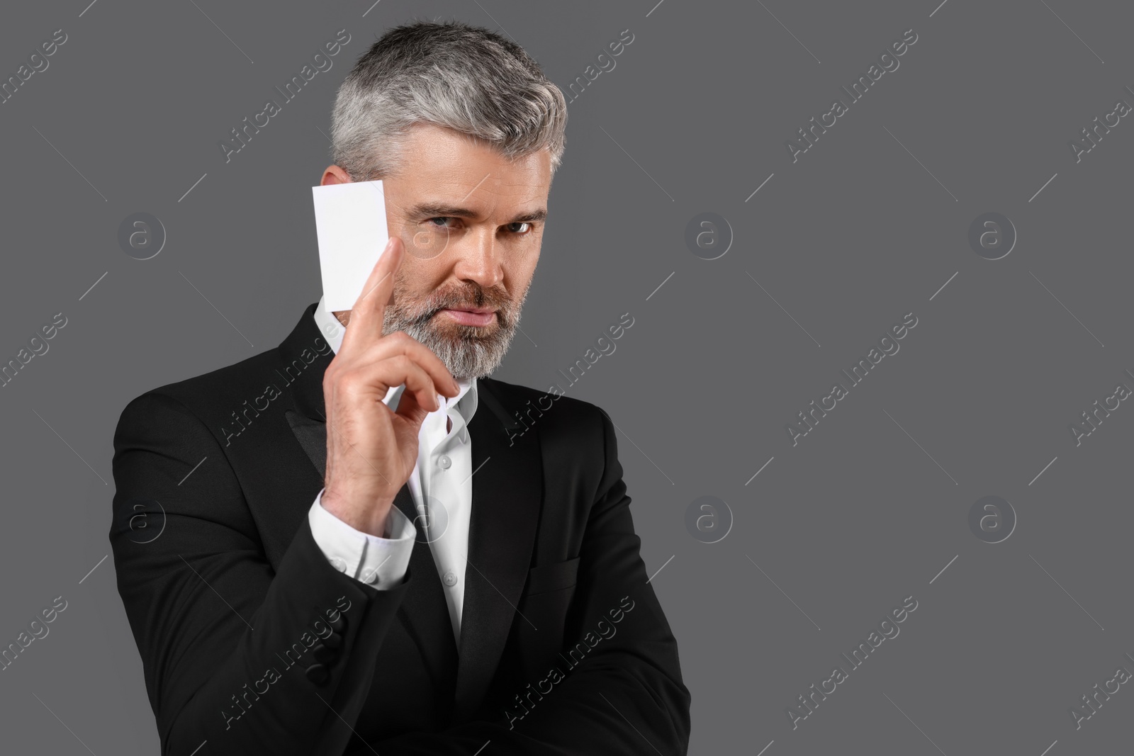 Photo of Handsome businessman holding blank business card on grey background. Space for text
