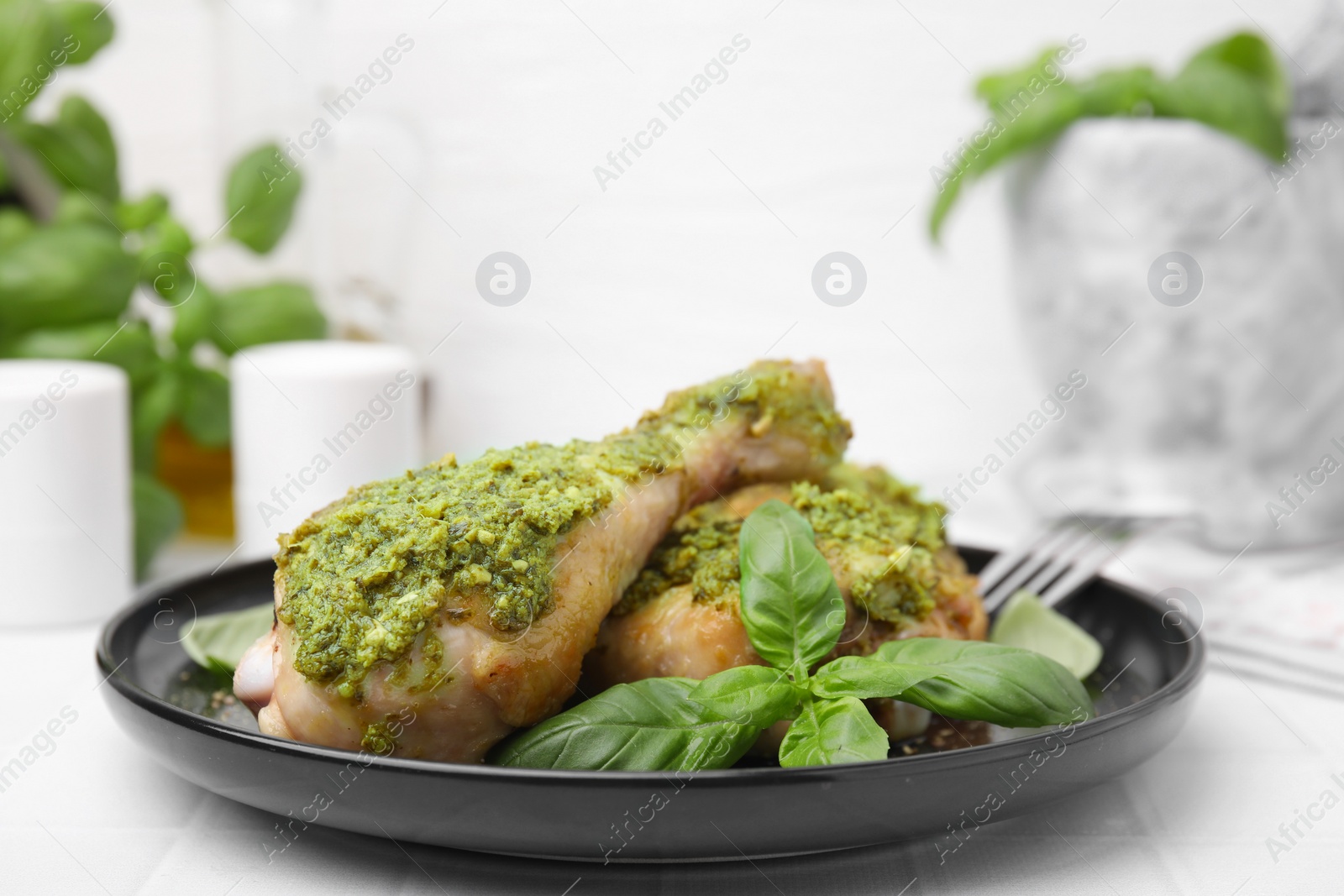 Photo of Delicious fried chicken drumsticks with pesto sauce and basil on white table, closeup