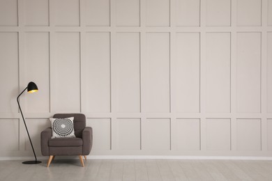 Photo of Grey armchair and lamp near empty molding wall indoors, space for text