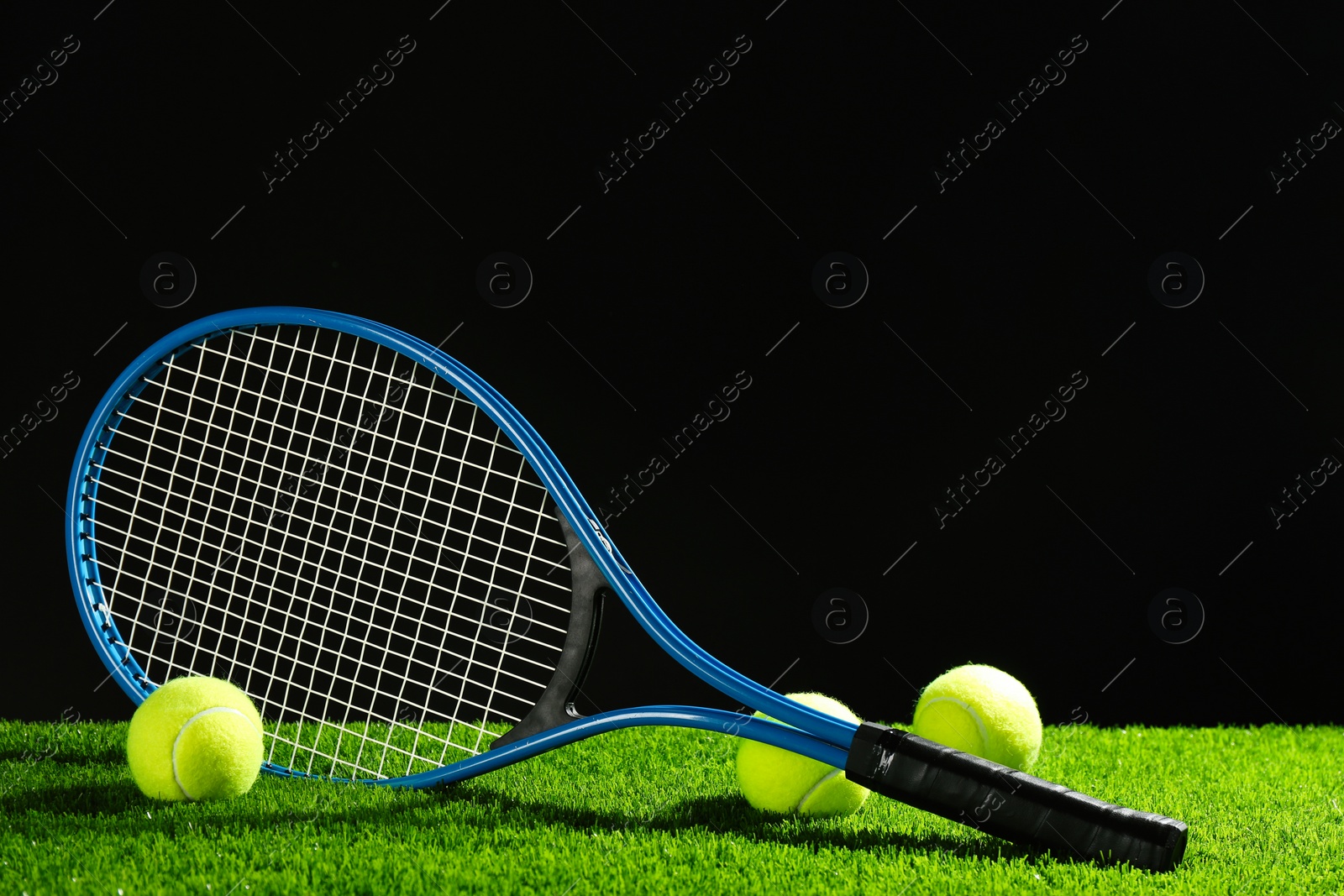 Photo of Tennis racket and balls on green grass against dark background. Space for text